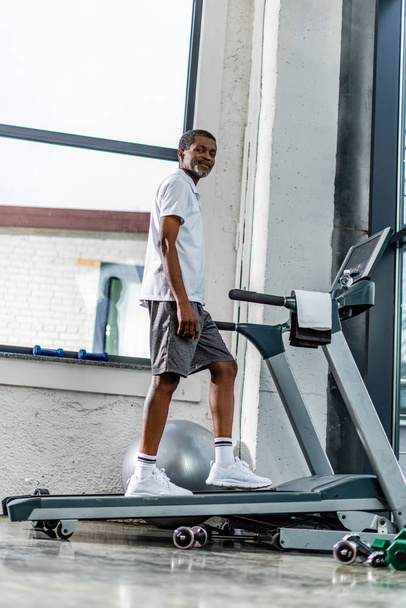 low angle view of smiling african american man exercising on treadmill at gym - Foto, Imagen