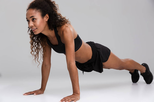 Portrait of an afro american young strong sportswoman doing plank exercise isolated over gray background - Photo, image