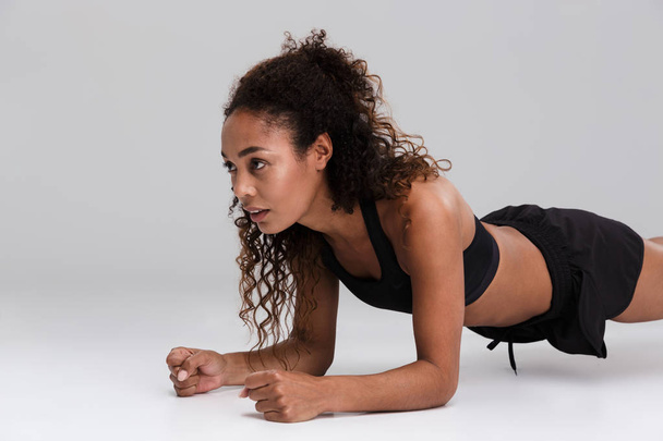 Portrait of an afro american young focused sportswoman doing plank exercise isolated over gray background - Foto, Bild