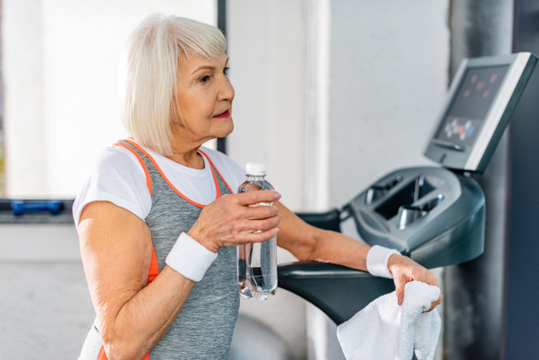 selective focus of senior sportswoman with water resting near treadmill at gym - Foto, Imagen