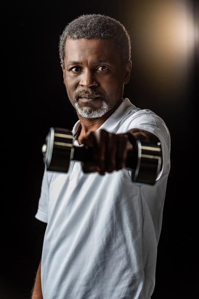 african american mature sportsman exercising with dumbbell on black  - Fotó, kép