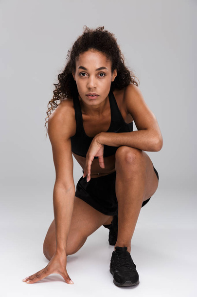 Beautiful african sportswoman sitting isolated over gray background, resting - Foto, Imagem