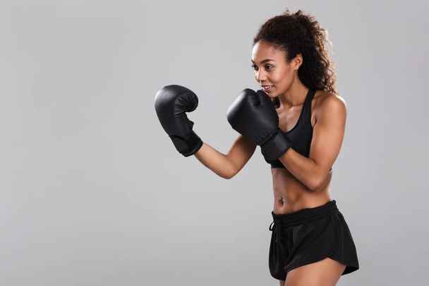 Portrait of an afro american smiling young sportswoman doing boxing isolated over gray background, looking away - Foto, afbeelding