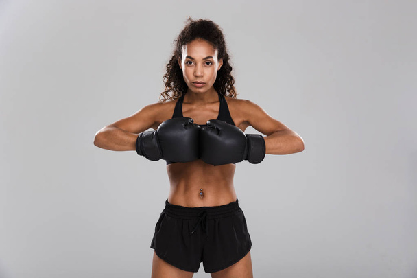 Portrait of an afro american confident young sportswoman doing boxing isolated over gray background - 写真・画像