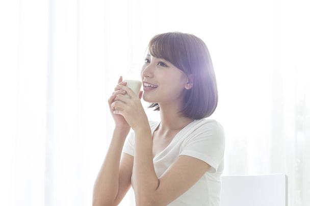 Молоді азіатські жінки проведення склянку молока і посміхаючись, хтось дивитися вбік - Фото, зображення