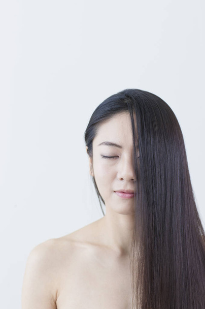 Young Asian woman with black long hair covering her face with her eyes closed - Фото, зображення