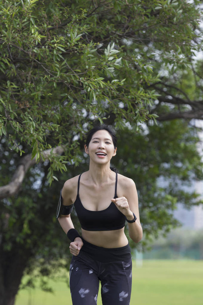 Young Asian woman smiling jogging in the park - 写真・画像