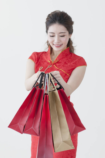 Young Chinese woman wearing a cheongsam holding some gifts and smiling at the camera - Фото, зображення