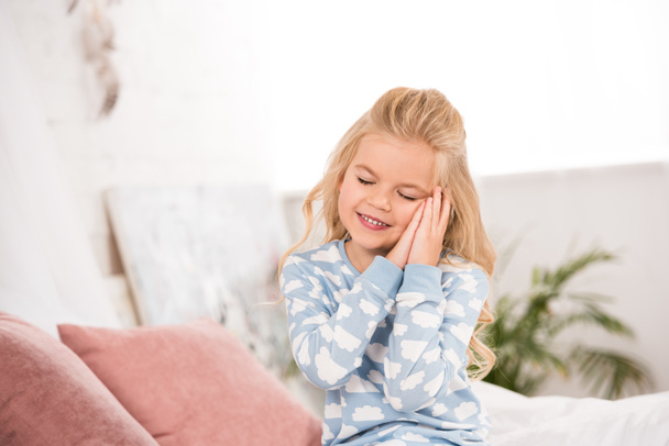 cute sleepy child sitting on bed with closed eyes  - Foto, afbeelding