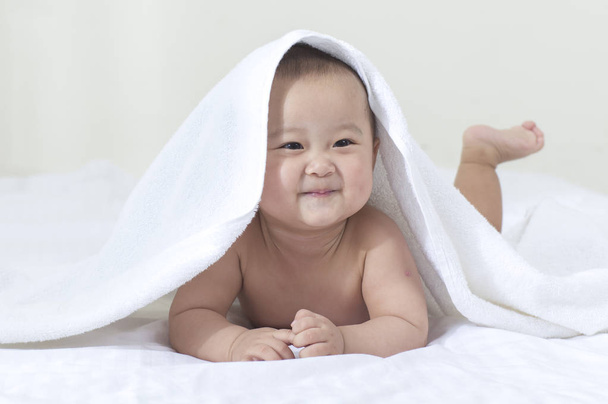 Young Asian baby hiding in the blanket and smiling looking away - 写真・画像