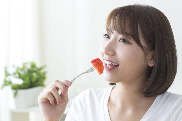 Young Asian woman smiling eating tomato - Foto, Imagem