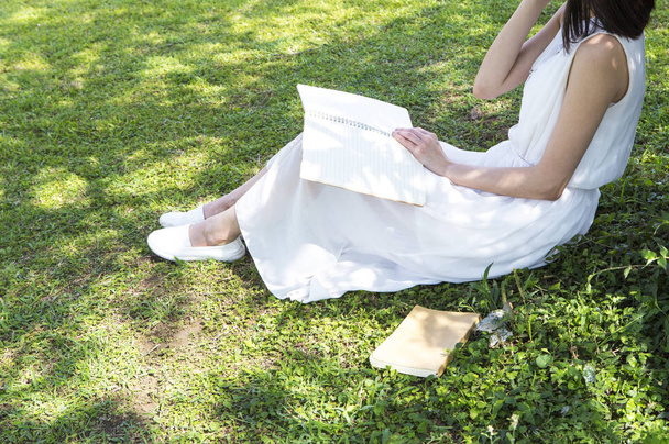 Ağacın altında bir kitap okuma beyaz bir elbise genç Asyalı kadın - Fotoğraf, Görsel