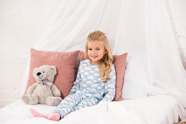 adorável criança sentada na cama com ursinho de pelúcia
 - Foto, Imagem
