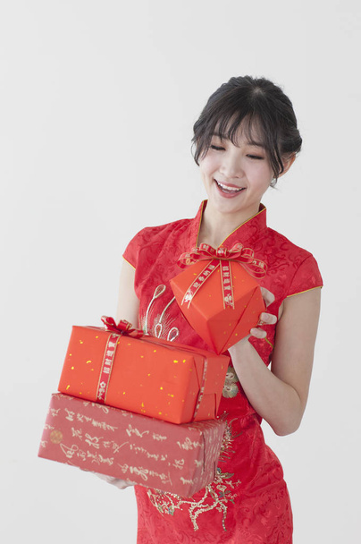 Young Chinese woman wearing a cheongsam holding some gifts and smiling at the camera - Foto, Imagem