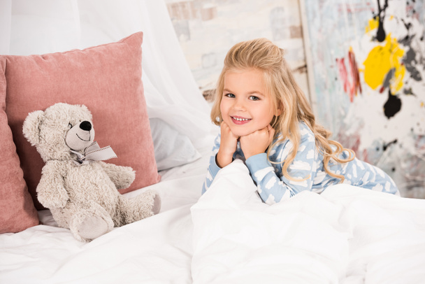 αξιολάτρευτο παιδί με αρκουδάκι στο κρεβάτι, βλέπουν τα φωτογραφικών μηχανών - Φωτογραφία, εικόνα