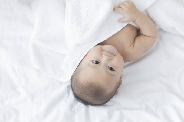 Young Asian baby lying on the bed and looking away - Foto, Imagen