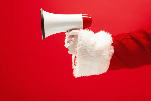 Hand of Santa Claus holding a megaphone on red background - Fotoğraf, Görsel