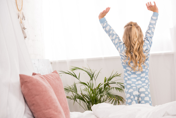 back view of kid in pajamas stretching near window in bedroom - Zdjęcie, obraz