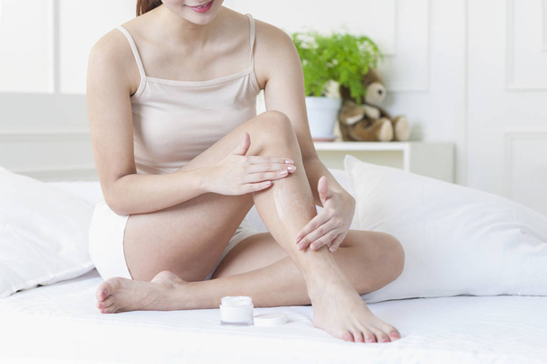 Young Asian woman putting lotion on her leg - Fotó, kép