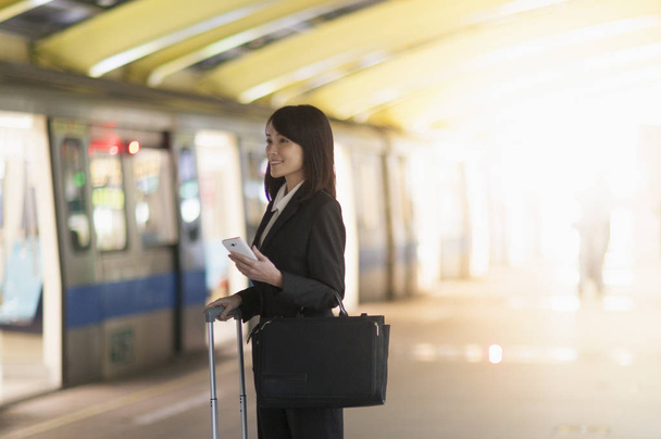 Mujer asiática joven con un traje sosteniendo una maleta esperando el tren
 - Foto, Imagen
