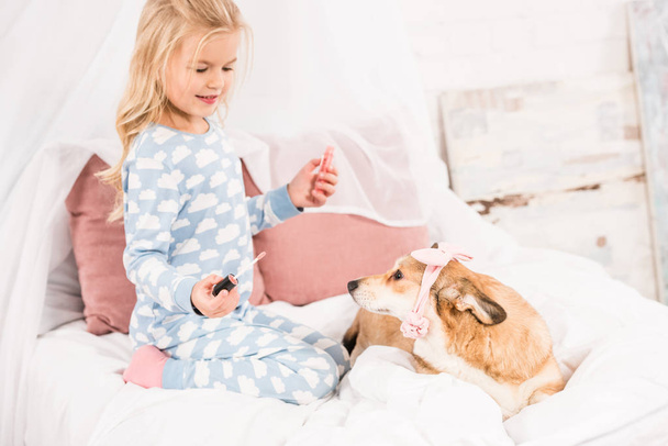 cute child with lip gloss looking at corgi dog with pink accessories - Фото, зображення