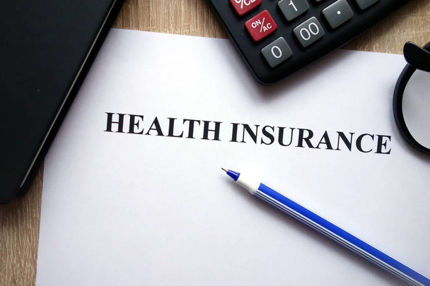 Health insurance document, calculator, pen and glasses on desk - Фото, зображення