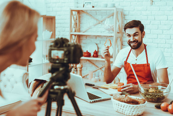 Blogger Makes a Video. Blogger is Smiling Beard Man. Video About a Cooking. Woman Operator Shoots a Video on Camera. Different Food on Table. Man Showing a Piece of Pepper. People in Studio Interior. - 写真・画像