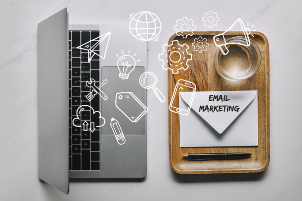 Pracoviště šablona s notebookem a dřevěný zásobník na obálky a vodou na bílém mramorovém pozadí s e-mailový marketing a ikony - Fotografie, Obrázek