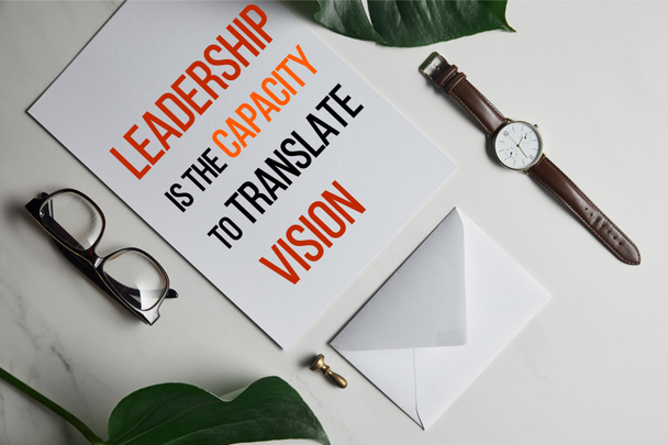 Karte mit "Führung ist die Fähigkeit, Vision zu übersetzen" Schriftzug, Uhr und Brille auf weißem Marmorhintergrund mit Monsterblättern   - Foto, Bild