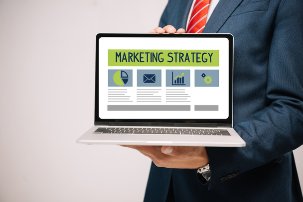 bijgesneden weergave van zakenman in pak presenteren laptop met marketing strategie geïsoleerd op grijs - Foto, afbeelding