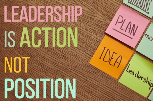 Top uitzicht op papier stickers met woorden plan, idee en leiderschap op houten tafelblad met "Leiderschap is actie, niet positie" belettering - Foto, afbeelding