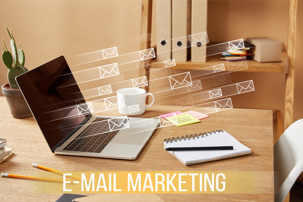 laptop met e-mail pictogrammen en "e-mail marketing" letters op houten tafel thuis - Foto, afbeelding