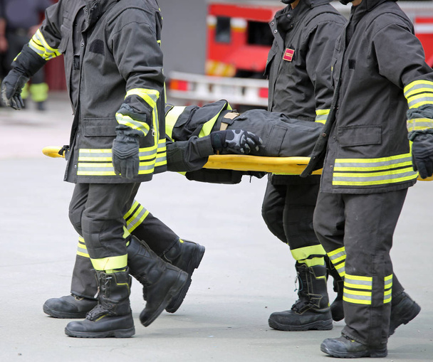 Brandweerlieden dragen een gewonde man op een brancard tijdens een oefening - Foto, afbeelding