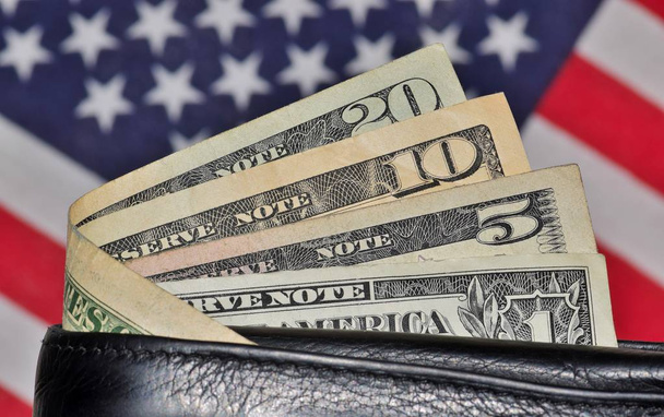 Wallet with several dollar bills sticking out of it with an American flag slightly blurred in the background behind it. - Photo, Image