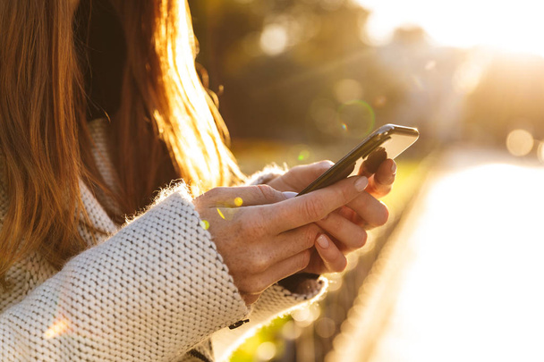 Обрізана фотографія рудої жінки, яка гуляє на відкритому повітрі, спілкуючись по мобільному телефону
. - Фото, зображення