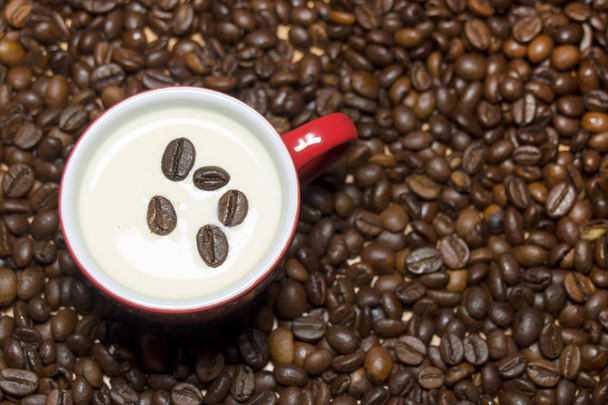 Hrnek na kávu s mlékem krém na dřevěný stůl s zrnková káva v šálku a kolem něj. - Fotografie, Obrázek