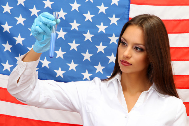 Portrait of female doctor or scientist showing and analyzing liquid in flask over American Flag background - Photo, image