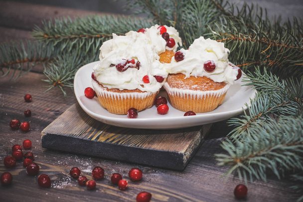年賀はがきの背景のお祭りの組成物。白いプレートに焼きたてケーキ赤い果実で飾られ、光の木製テーブルの上にスプルースの小枝で飾られた赤い果実をトッピング プレートとホワイト クリームをホイップ クリーム. - 写真・画像