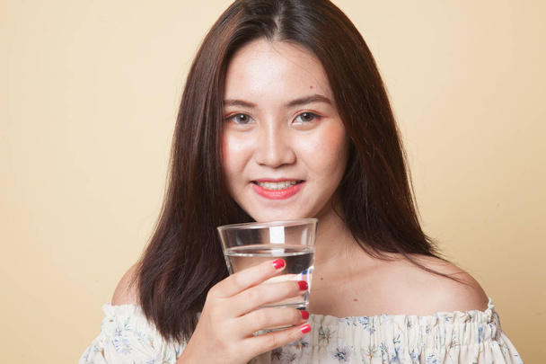 Young Asian woman with a glass of drinking water on beige background - Foto, afbeelding