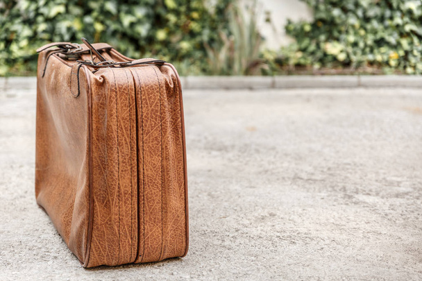 Vintage brown suitcase located on the left side of the photograph, placed on the floor of a patio - Fotografie, Obrázek