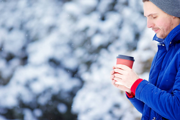 Młody człowiek kaukaski picia kawy w zamarzniętym zimą dzień na zewnątrz - Zdjęcie, obraz