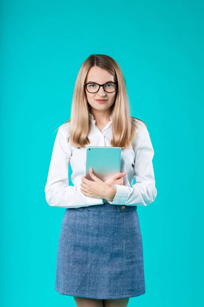 Портрет молодой кавказской женщины-работницы учитель наставничества в белой рубашке офисный стиль длинные волосы с планшетом в руке использует технологии изолированных ярко-голубой фон
. - Фото, изображение