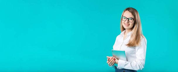 Portret jonge Kaukasische vrouw werknemer leraar trainer mentoring in wit overhemd office stijl lange haren met een tablet in de hand gebruikt technologie geïsoleerd helder blauwe achtergrondkleur. - Foto, afbeelding