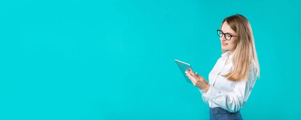 Retrato joven mujer caucásica profesora formadora mentoría en camisa blanca estilo oficina pelo largo con una tableta en la mano utiliza la tecnología aislada de color brillante fondo azul
. - Foto, imagen