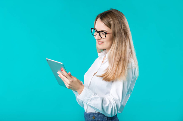 Portrait young caucasian woman worker teacher trainer mentoring in white shirt office style long hair with a tablet in hand uses technology isolated bright color blue background. - 写真・画像