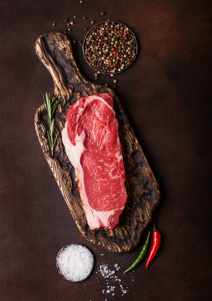 Raw sirloin beef steak on old chopping board with salt and pepper on rusty background. - Photo, image