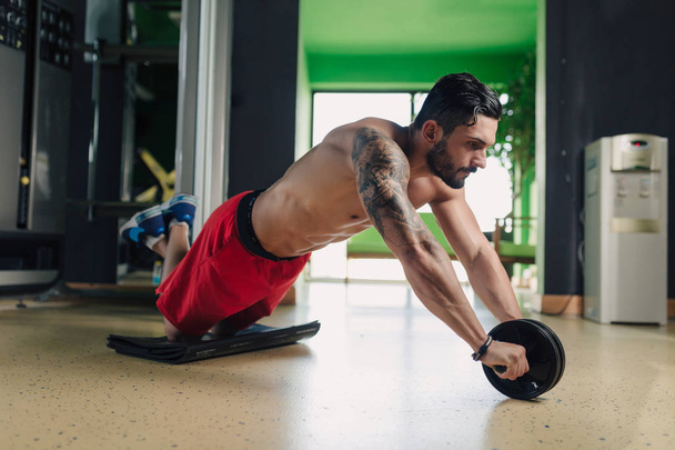 Сильный мужчина в спортзале делает упражнения на животе
 - Фото, изображение