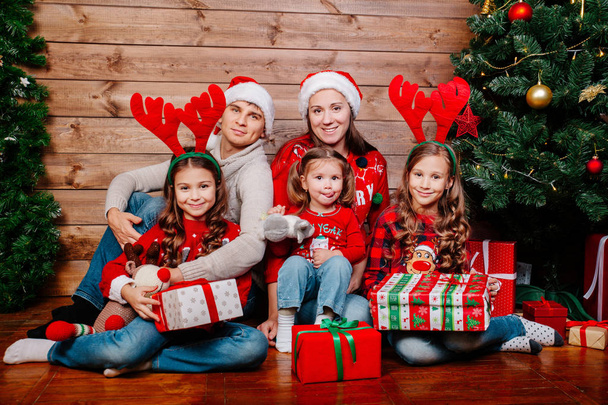 Big smiling family in santa hats with many gift boxes sittting near Christmas tree at home. Merry Christmas and Happy Holidays - Photo, image