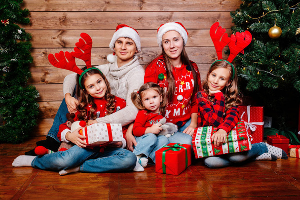 Big smiling family in santa hats with many gift boxes sittting near Christmas tree at home. Merry Christmas and Happy Holidays - Photo, image