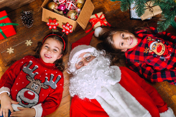 Twee meisjes en Santa liggen op de vloer thuis in de buurt van de kerstboom - Foto, afbeelding